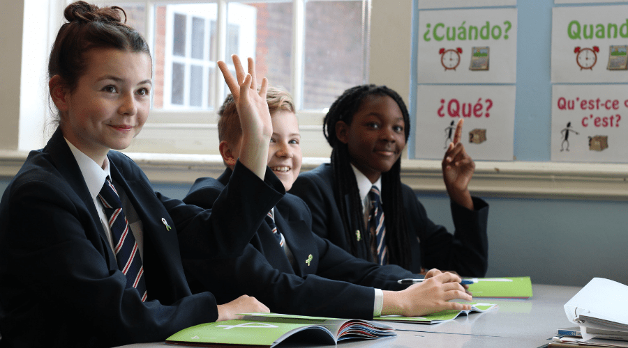 Pupils sat in a classroom, with their hands raised